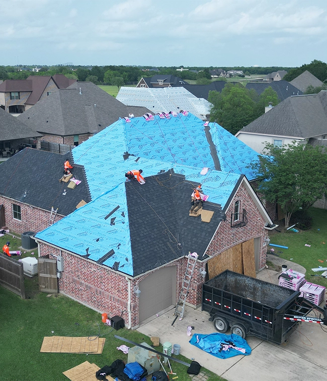Roof replacement in progress on a residential home in Greater Houston with roofing crews installing new shingles and underlayment.